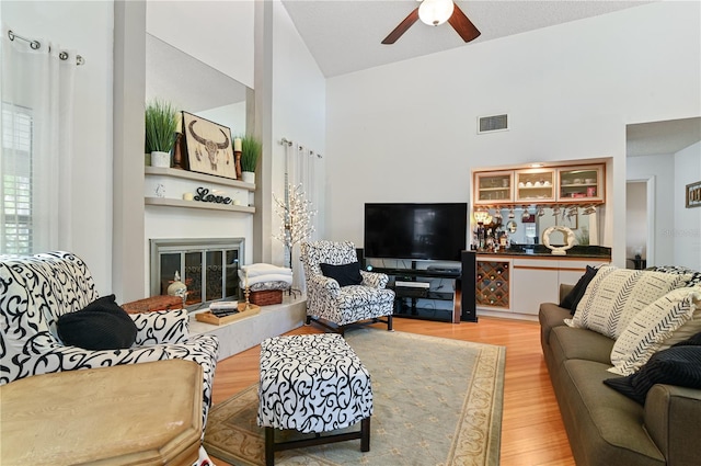 living room featuring ceiling fan, high vaulted ceiling, and light hardwood / wood-style flooring