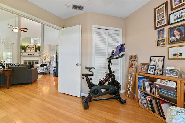 exercise area with ceiling fan, a textured ceiling, and light wood-type flooring