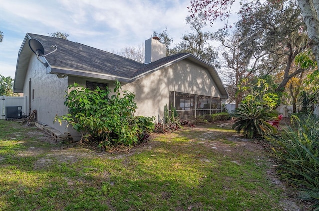 rear view of house with central AC unit, a lawn, and a sunroom