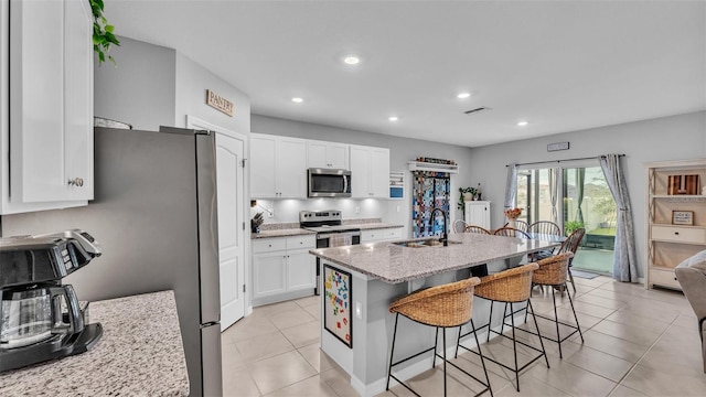 kitchen featuring a breakfast bar area, white cabinets, a kitchen island with sink, light stone counters, and stainless steel appliances