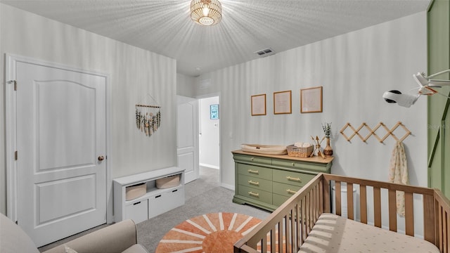 bedroom featuring a nursery area, light carpet, and a textured ceiling