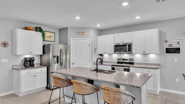 kitchen featuring light stone countertops, a breakfast bar area, an island with sink, appliances with stainless steel finishes, and a sink