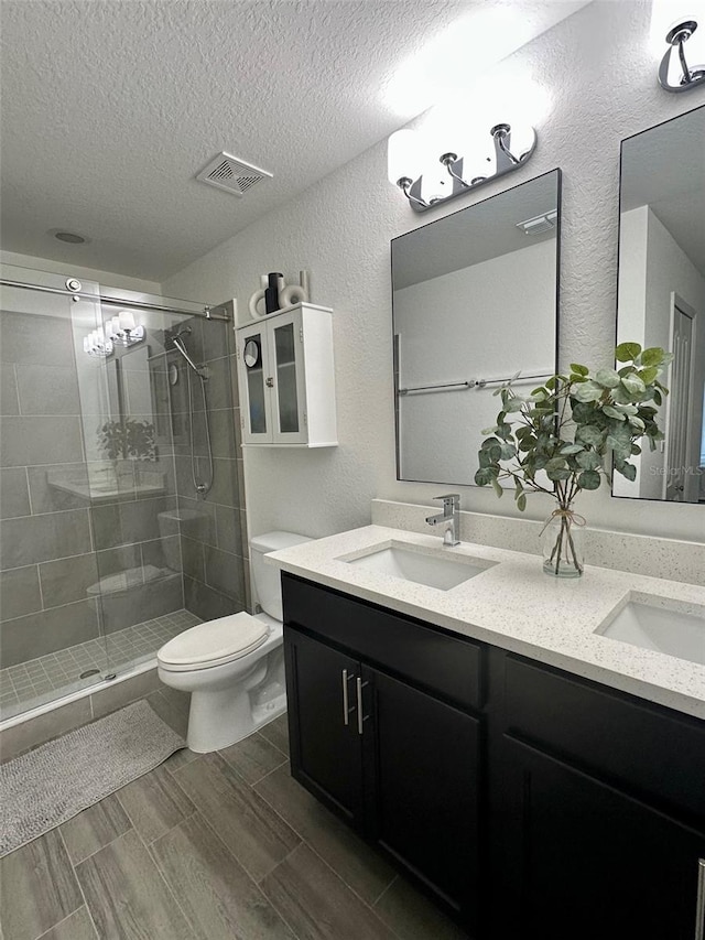 bathroom featuring vanity, toilet, a shower with door, and a textured ceiling