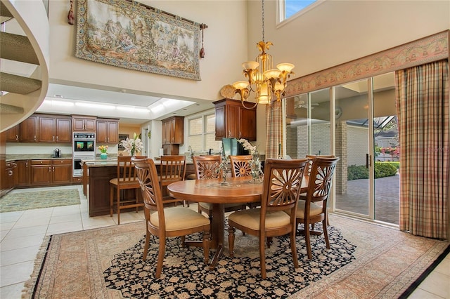 tiled dining space with plenty of natural light, a towering ceiling, and an inviting chandelier