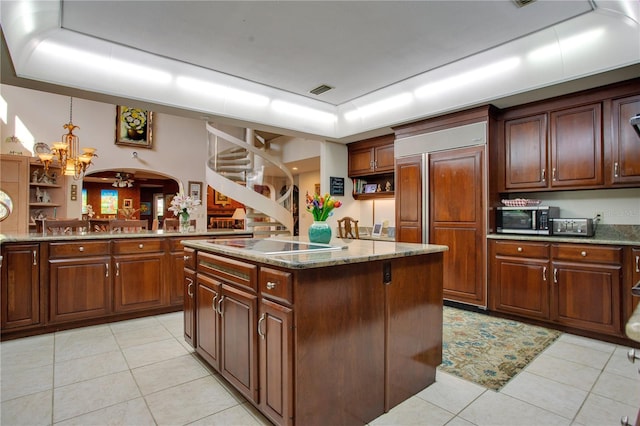 kitchen featuring paneled built in refrigerator, a center island, light tile patterned floors, and a tray ceiling