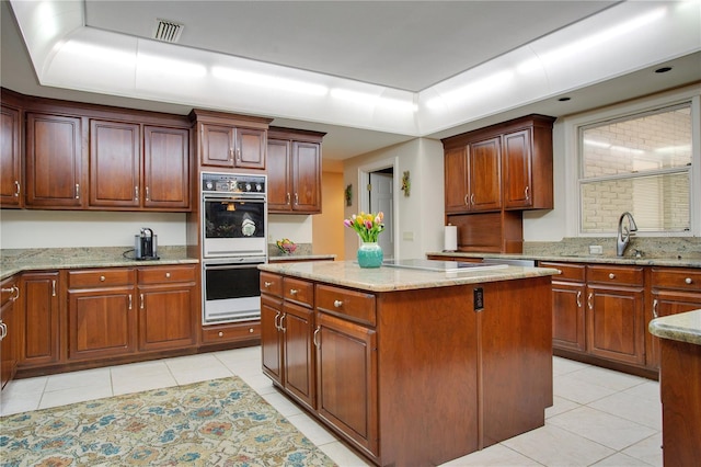 kitchen featuring light tile patterned floors, white double oven, light stone counters, a kitchen island, and cooktop