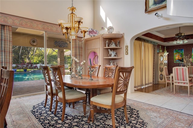 dining area with ceiling fan with notable chandelier, ornamental molding, a towering ceiling, and light tile patterned flooring