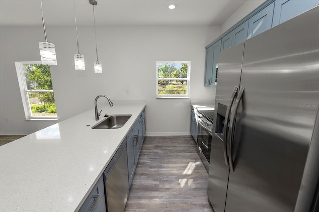 kitchen featuring appliances with stainless steel finishes, sink, hanging light fixtures, light stone counters, and dark wood-type flooring