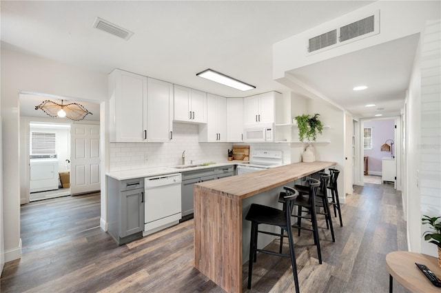 kitchen with a breakfast bar, sink, white cabinetry, wooden counters, and white appliances