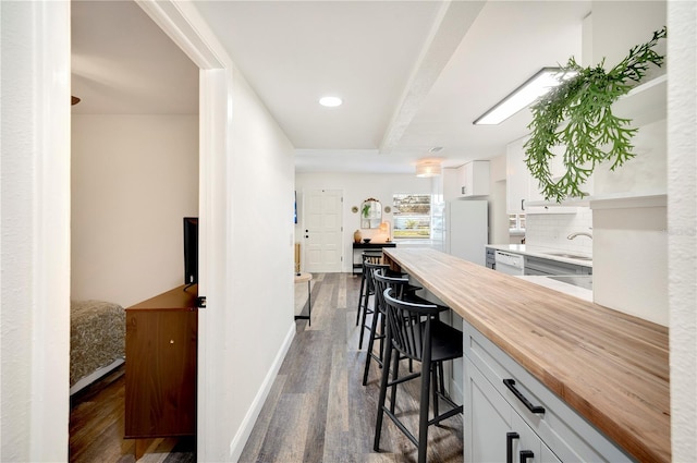 kitchen with butcher block countertops, white appliances, dark wood-type flooring, a kitchen breakfast bar, and white cabinets