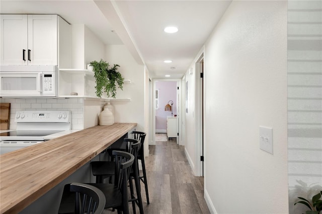 interior space with butcher block countertops, tasteful backsplash, white cabinetry, a breakfast bar area, and white appliances