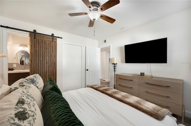 bedroom with ceiling fan, a barn door, ensuite bath, and a closet