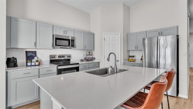 kitchen featuring sink, appliances with stainless steel finishes, a kitchen island with sink, a kitchen breakfast bar, and light stone countertops