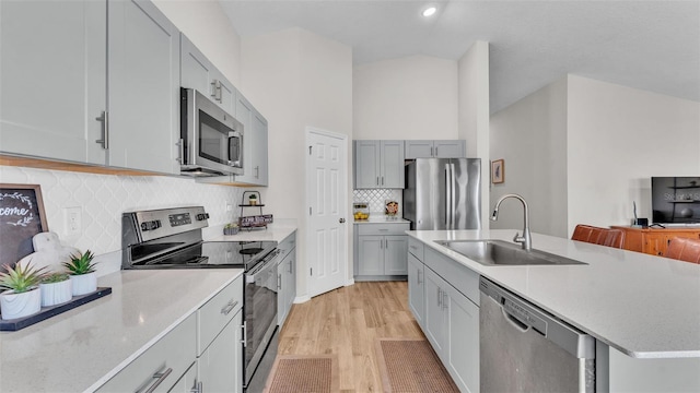 kitchen with sink, tasteful backsplash, light hardwood / wood-style flooring, an island with sink, and stainless steel appliances