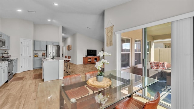 dining room with vaulted ceiling, sink, and light hardwood / wood-style floors