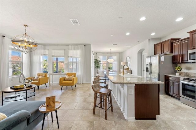 kitchen with sink, hanging light fixtures, stainless steel appliances, a center island with sink, and an inviting chandelier