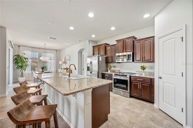 kitchen with appliances with stainless steel finishes, sink, a breakfast bar area, hanging light fixtures, and a kitchen island with sink