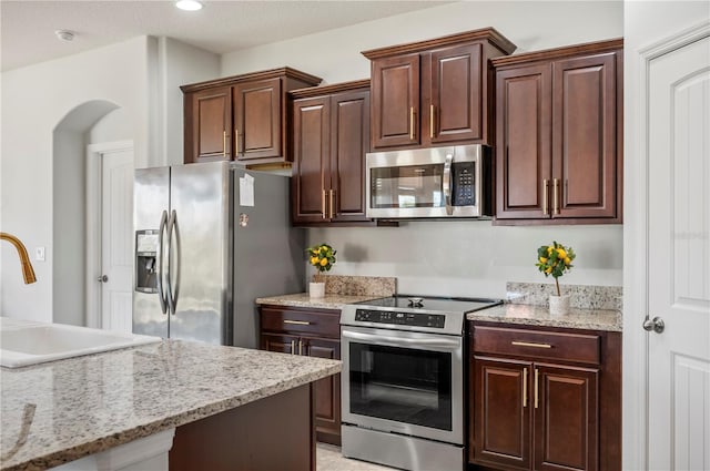 kitchen featuring dark brown cabinetry, sink, light stone countertops, and appliances with stainless steel finishes