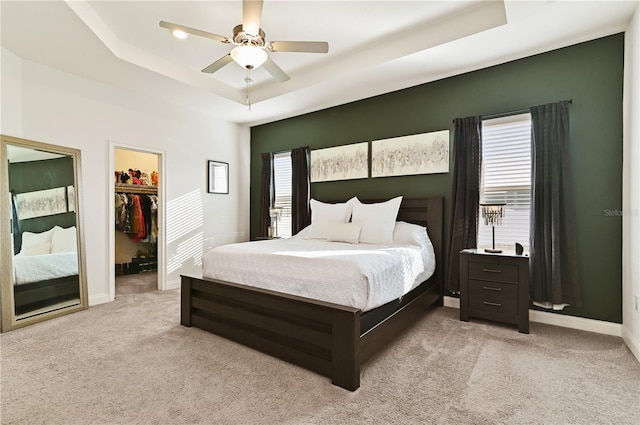 bedroom featuring light carpet, a tray ceiling, a walk in closet, and ceiling fan