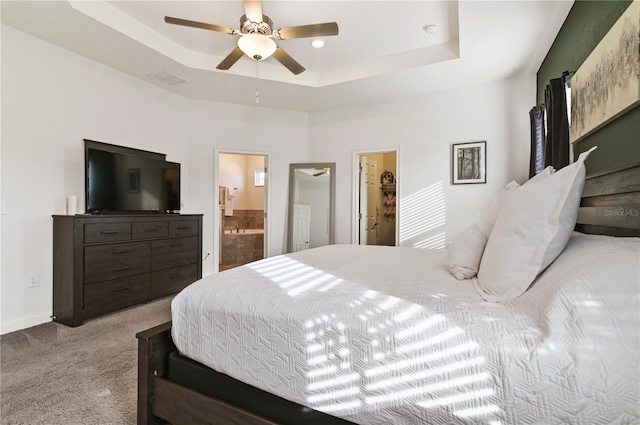 carpeted bedroom with a tray ceiling, ceiling fan, and ensuite bathroom