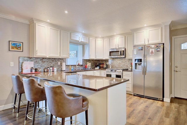 kitchen featuring white cabinetry, appliances with stainless steel finishes, a kitchen bar, and kitchen peninsula