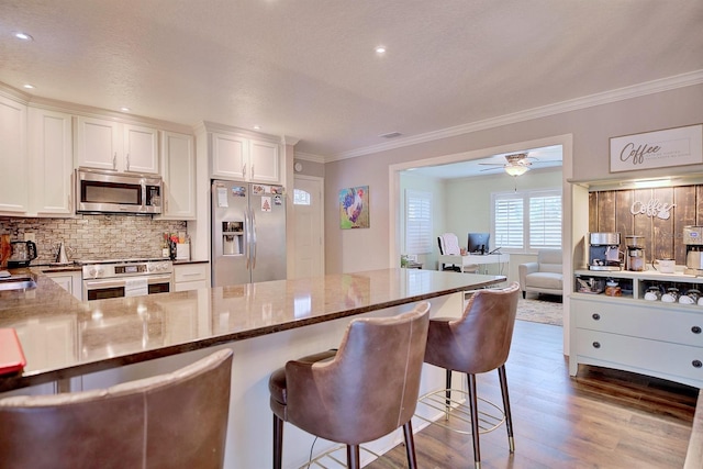 kitchen featuring stainless steel appliances, white cabinetry, a kitchen bar, and dark stone counters