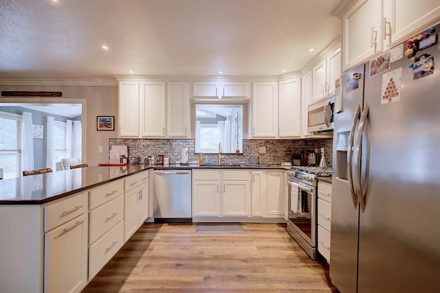 kitchen with light hardwood / wood-style flooring, appliances with stainless steel finishes, tasteful backsplash, white cabinets, and kitchen peninsula