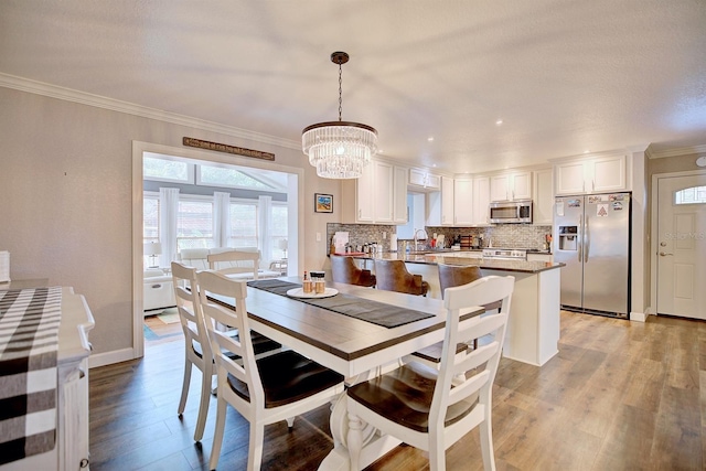 dining area featuring a notable chandelier, ornamental molding, sink, and light wood-type flooring