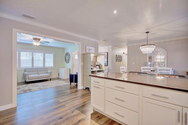 kitchen featuring crown molding, hanging light fixtures, hardwood / wood-style flooring, ceiling fan with notable chandelier, and white cabinets