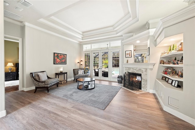 living room with french doors, crown molding, light hardwood / wood-style flooring, and a tray ceiling