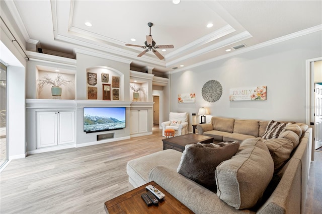 living room featuring a raised ceiling, ceiling fan, crown molding, and light wood-type flooring