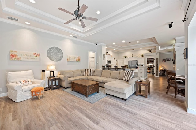 living room with ceiling fan, ornamental molding, a tray ceiling, and light hardwood / wood-style flooring