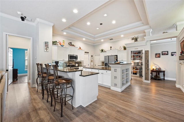 kitchen with appliances with stainless steel finishes, white cabinetry, a breakfast bar area, hardwood / wood-style flooring, and a center island