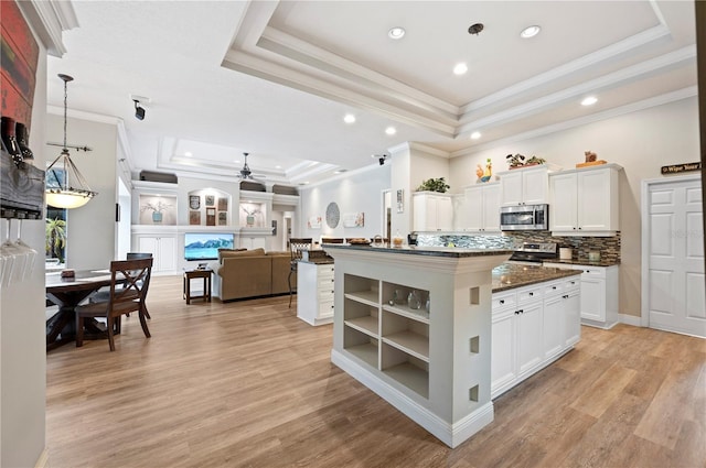 kitchen with appliances with stainless steel finishes, decorative light fixtures, white cabinetry, a tray ceiling, and a center island with sink