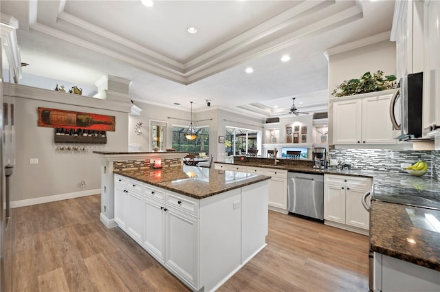 kitchen featuring decorative light fixtures, a tray ceiling, a kitchen island, stainless steel appliances, and white cabinets