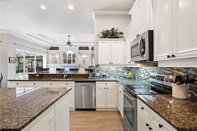 kitchen featuring white cabinetry, ornamental molding, dark stone counters, and appliances with stainless steel finishes