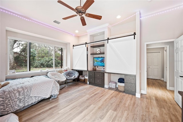 bedroom featuring ceiling fan, a barn door, and light hardwood / wood-style floors