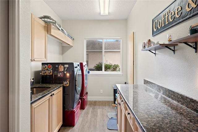 kitchen featuring sink, dark stone countertops, a textured ceiling, separate washer and dryer, and light wood-type flooring