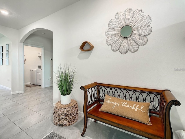 hallway with baseboards, arched walkways, separate washer and dryer, and tile patterned flooring