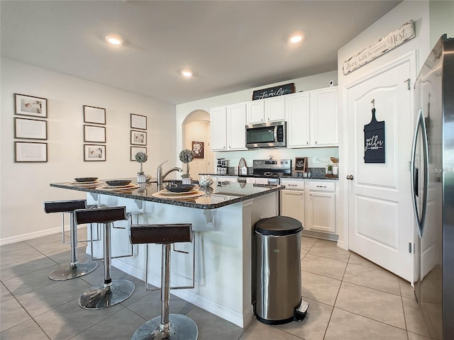 kitchen featuring a breakfast bar, light tile patterned floors, stainless steel appliances, arched walkways, and white cabinetry