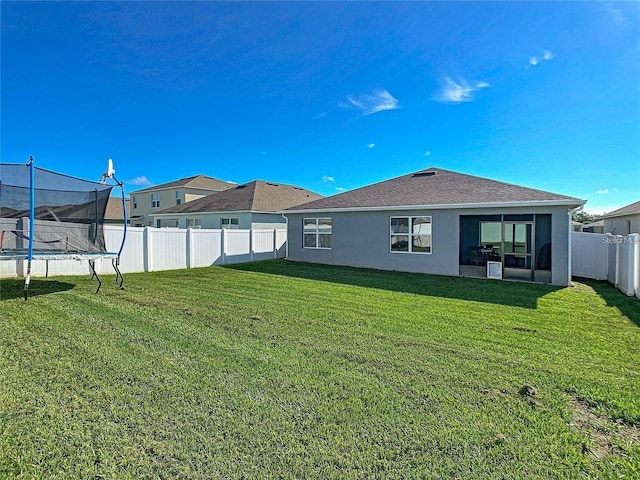 back of house with a fenced backyard, a lawn, a trampoline, and stucco siding