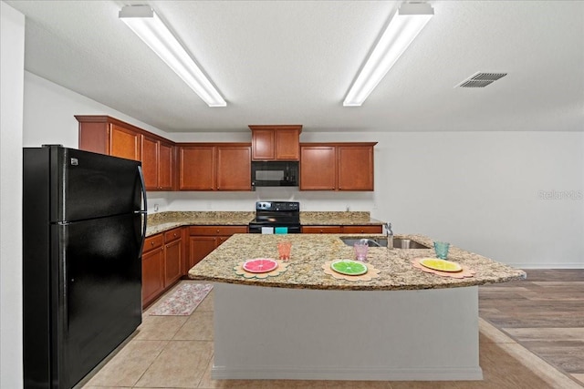 kitchen with an island with sink, light stone countertops, sink, and black appliances