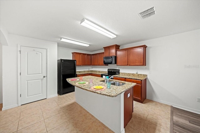 kitchen with sink, light tile patterned floors, a kitchen island with sink, black appliances, and light stone countertops