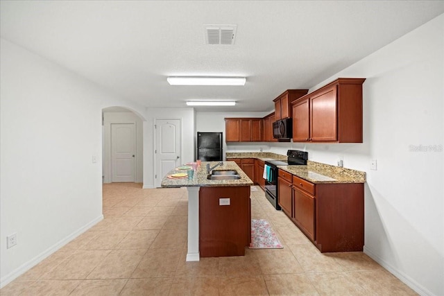 kitchen with an island with sink, sink, light tile patterned floors, light stone counters, and black appliances