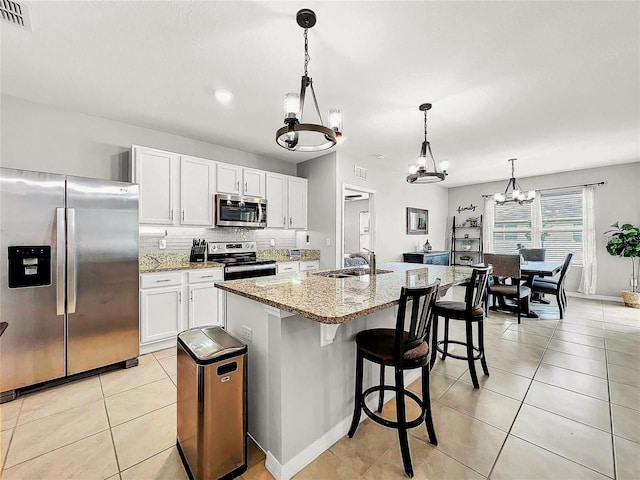 kitchen with appliances with stainless steel finishes, sink, white cabinets, hanging light fixtures, and a center island with sink