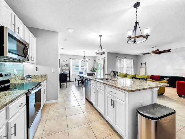 kitchen with appliances with stainless steel finishes, a kitchen island with sink, white cabinets, and decorative light fixtures