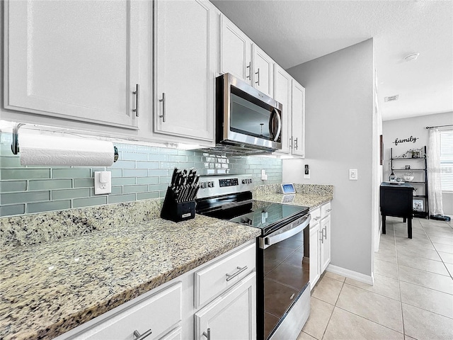 kitchen with light tile patterned floors, light stone countertops, white cabinets, and appliances with stainless steel finishes