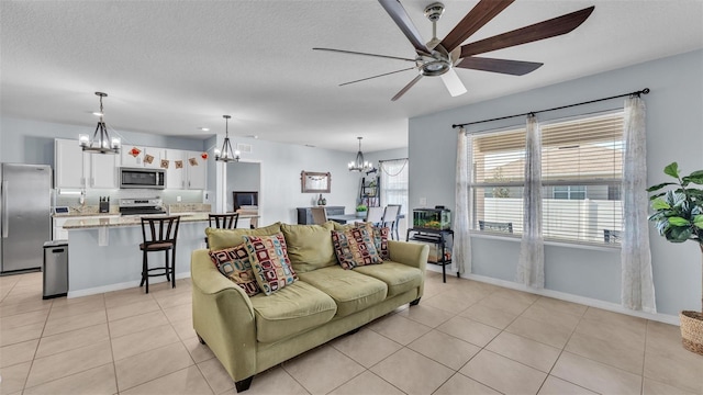 living area featuring a textured ceiling, ceiling fan with notable chandelier, light tile patterned flooring, and baseboards