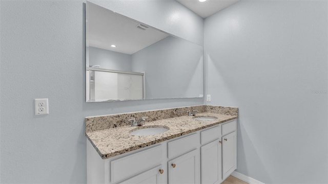 bathroom featuring a shower with shower door, a sink, baseboards, and double vanity