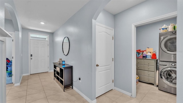 entrance foyer with arched walkways, stacked washer and dryer, light tile patterned flooring, and baseboards